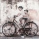 A realist street art wall mural of two life-size children positioned to appear as if they are riding an actual bicycle that is parked on a city sidewalk.